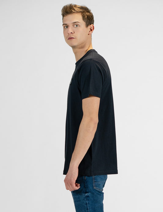 This image shows a side pose of a man wearing a classic dark navy crew-neck t-shirt paired with blue jeans.