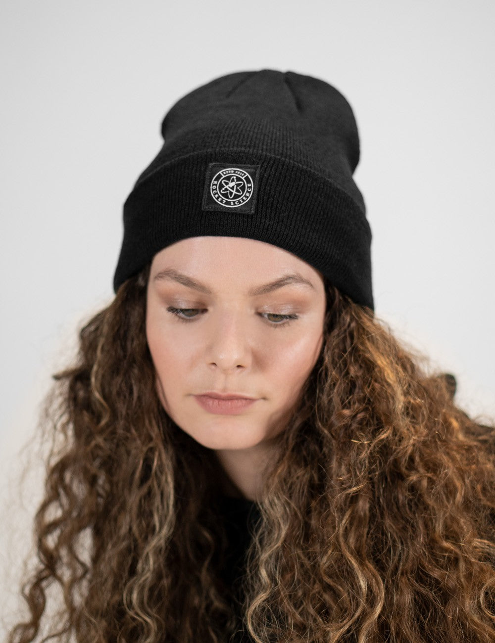 Woman showcasing a black heavy-knit beanie with a Rocket Science logo on the front.