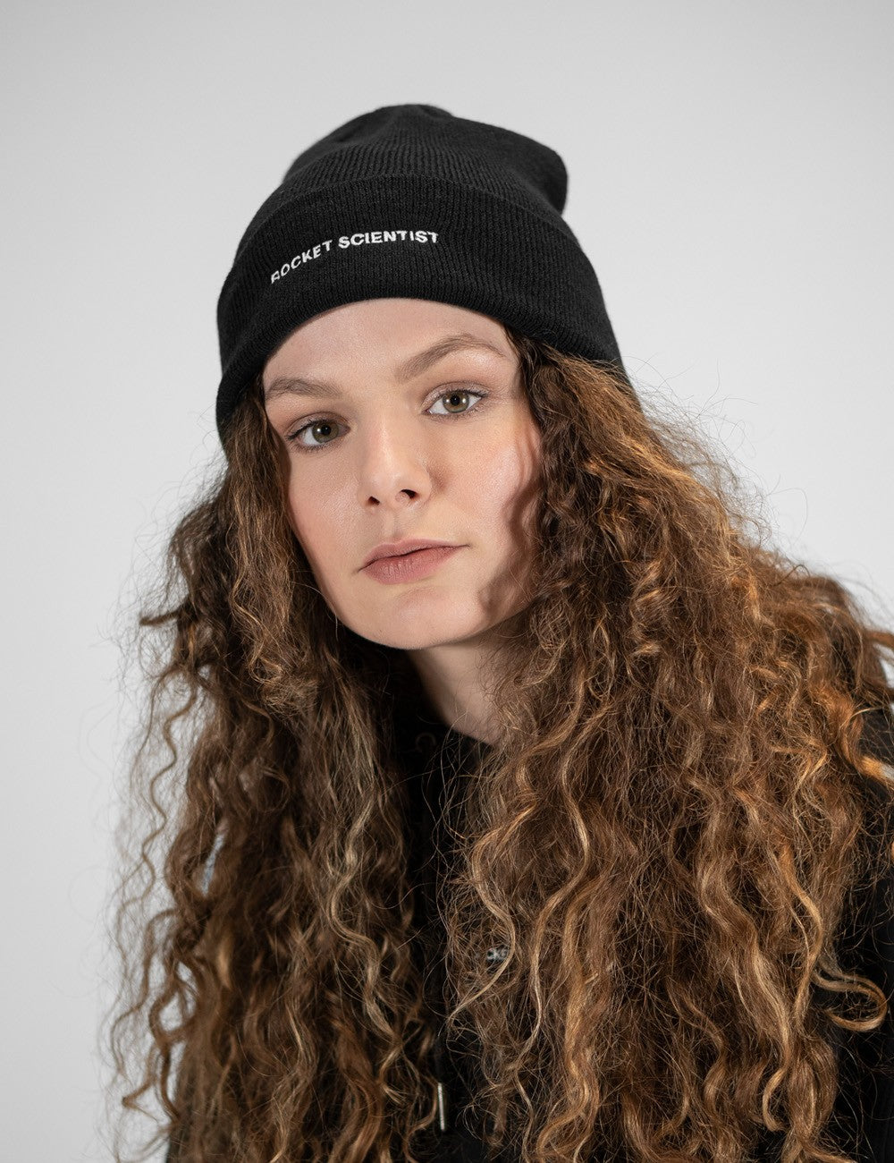 Woman showcasing a black heavy-knit beanie with a Rocket Science logo on the front

