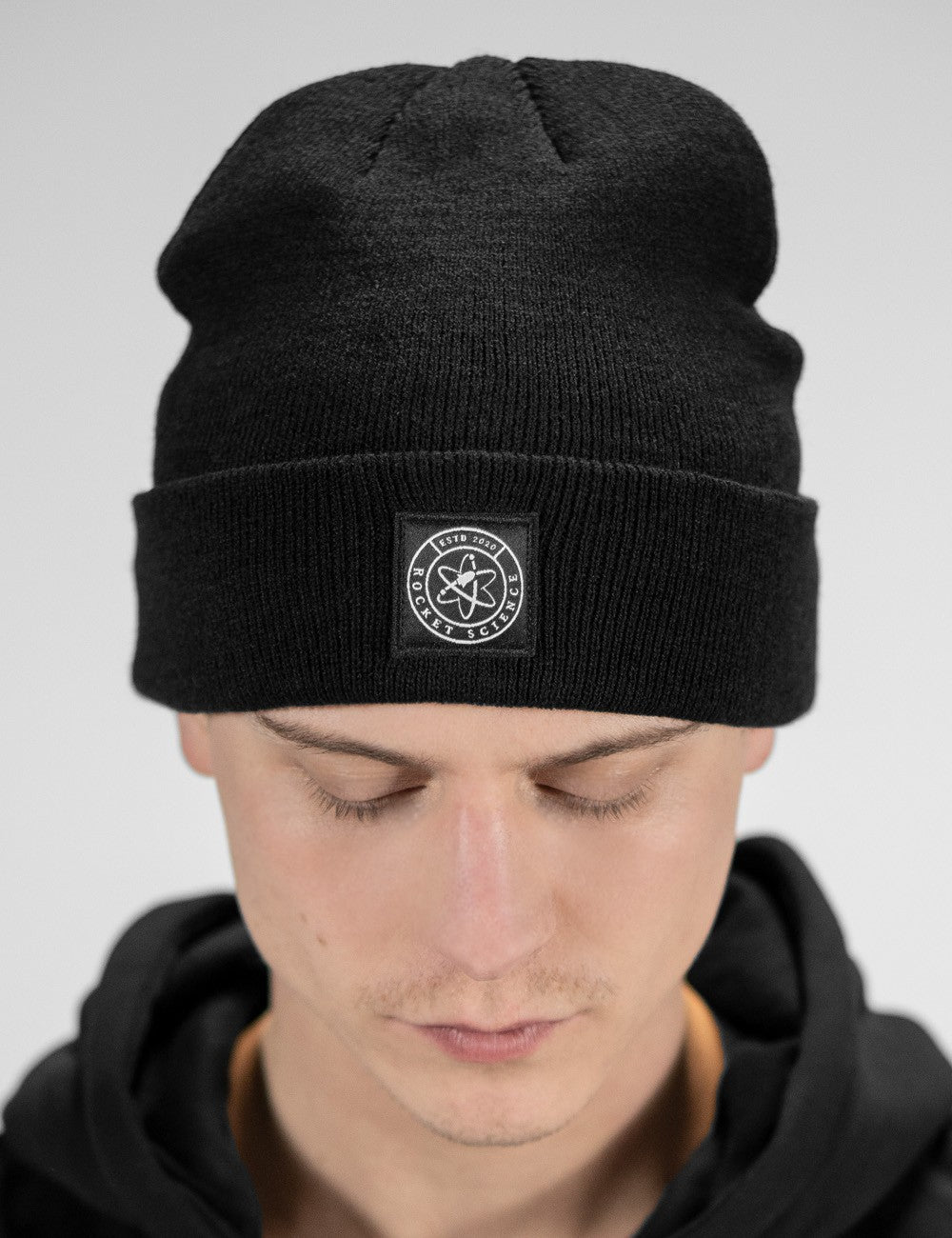 Man showcasing a black heavy-knit beanie with a Rocket Science logo on the front
