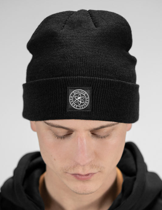 Man showcasing a black heavy-knit beanie with a Rocket Science logo on the front

