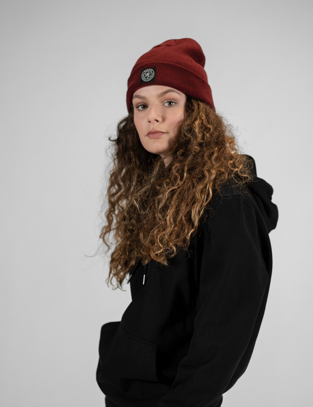 Woman showcasing a burgundy heavy-knit beanie with a Rocket Science logo on the front.