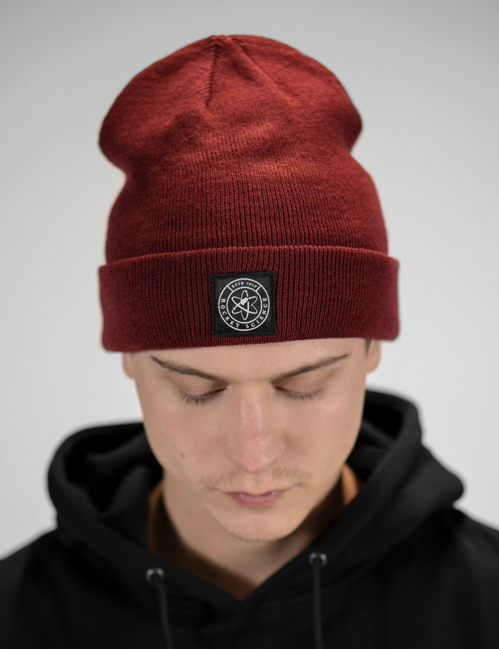 Man showcasing a burgundy heavy-knit beanie with a Rocket Science logo on the front.