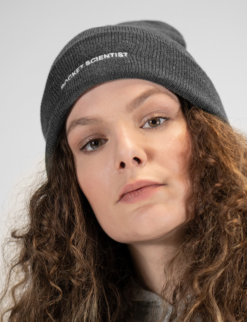 Woman showcasing a charcoal heavy-knit beanie with a Rocket Science logo on the front.