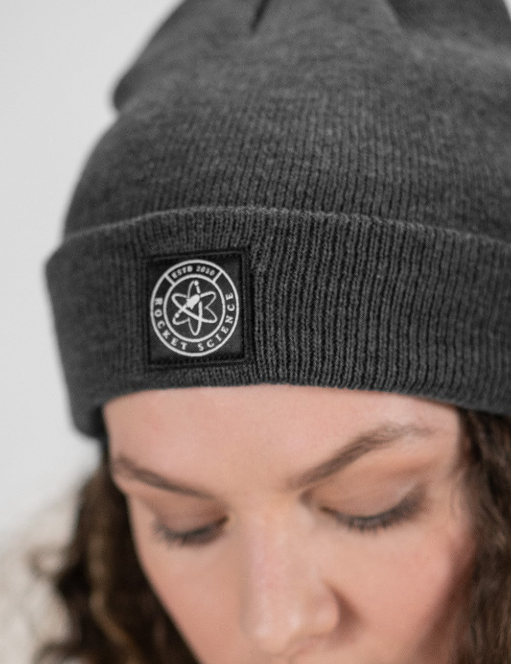 Woman showcasing a charcoal heavy-knit beanie with a Rocket Science logo on the front.