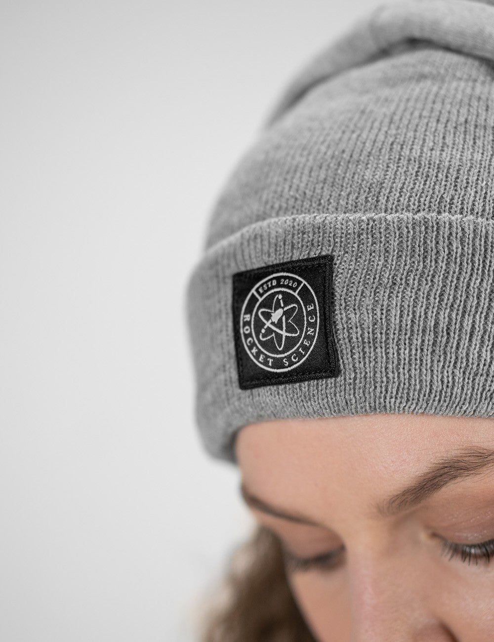 Woman showcasing a heather gray heavy-knit beanie with a Rocket Science logo on the front.