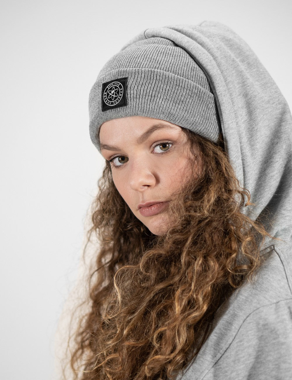 Woman showcasing a heather gray heavy-knit beanie with a Rocket Science logo on the front.