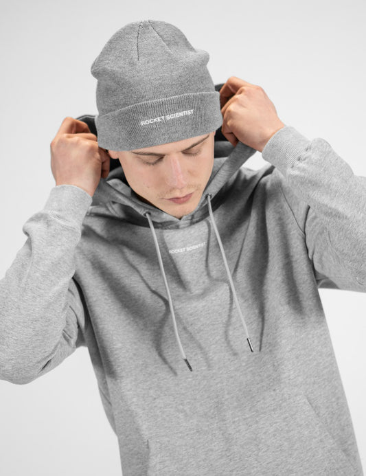 Man showcasing a heather gray heavy-knit beanie with the words “Rocket Scientist” on the front.