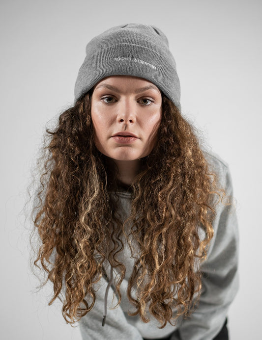 Woman showcasing a heather gray heavy-knit beanie with the words “Rocket Scientist” on the front.