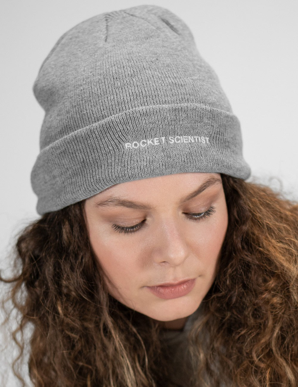 Woman showcasing a heather gray heavy-knit beanie with the words “Rocket Scientist” on the front.