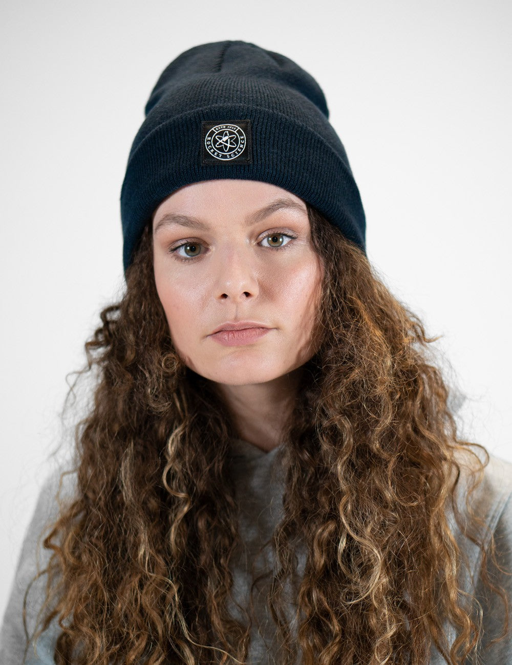 Woman showcasing a navy heavy-knit beanie with a Rocket Science logo on the front.