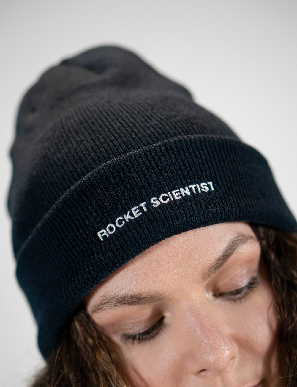 Woman showcasing a navy heavy-knit beanie with the words “Rocket Scientist” on the front.