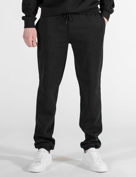 This image shows a front pose of a person wearing black sweatpants, paired with white sneakers.