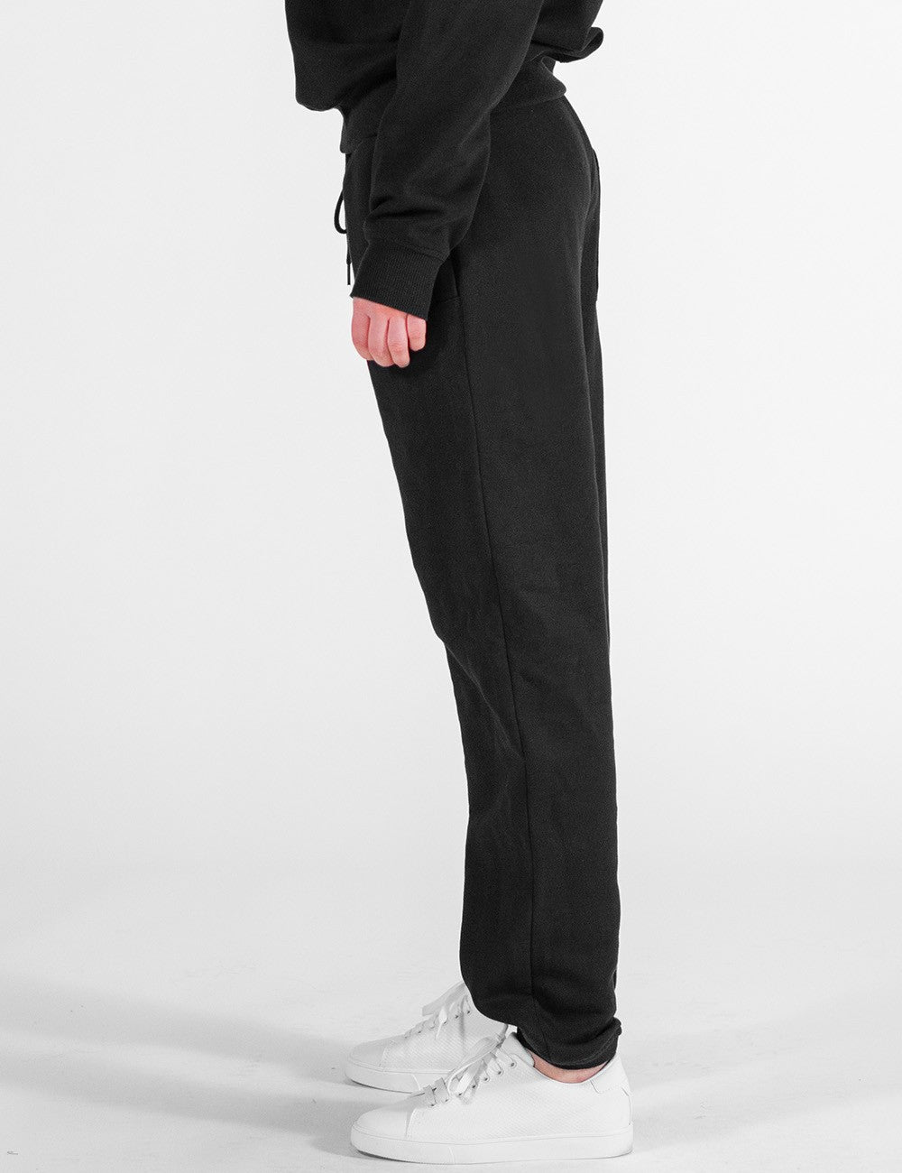 The image shows a side pose of a pair of black sweatpants with an elastic waistband, side pockets