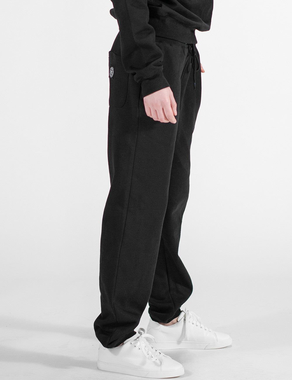 The image shows black sweatpants with an elastic waistband and cuffs paired with white sneakers. 