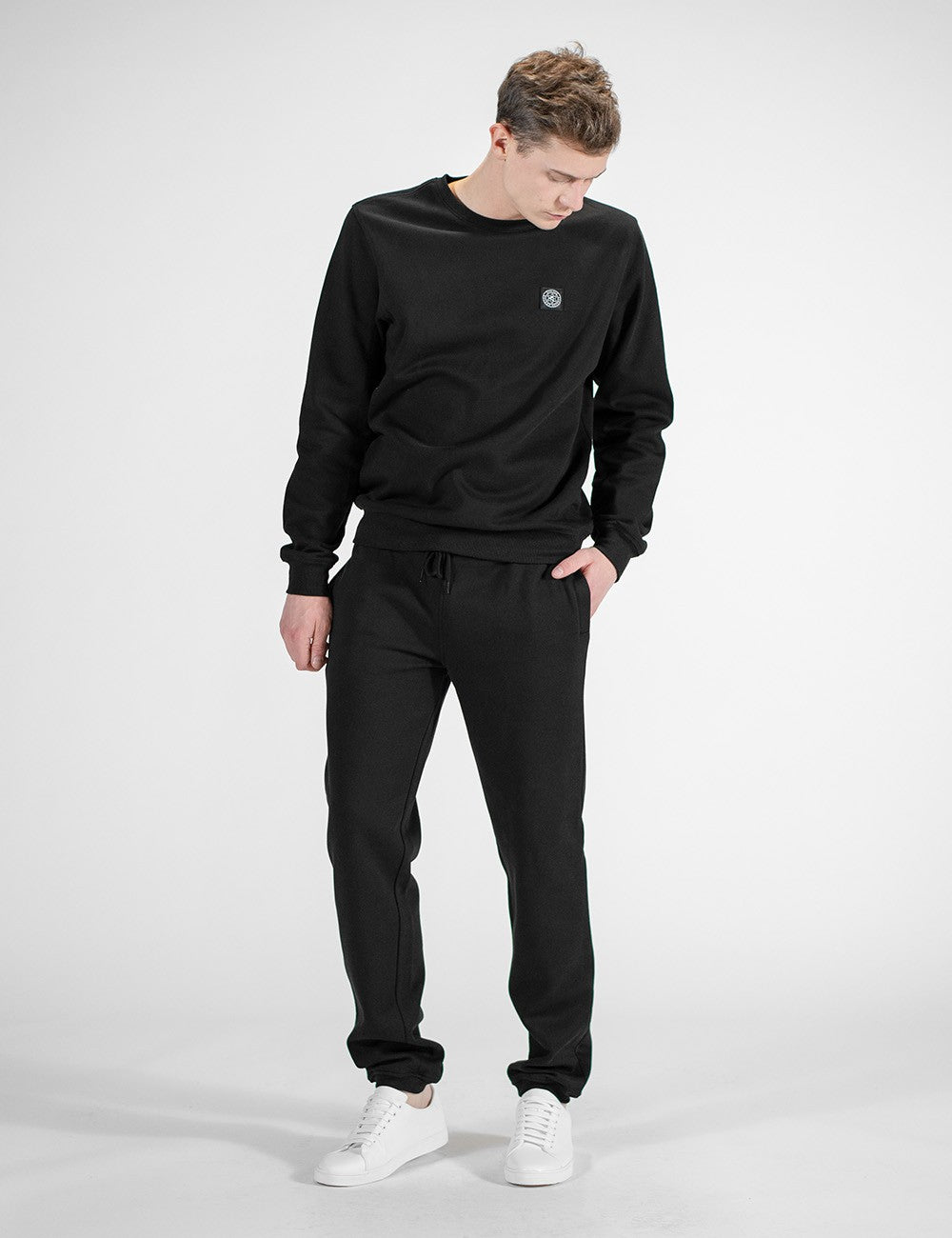This image shows a person wearing a casual black crew-neck sweatshirt and matching black sweatpants, paired with white sneakers.