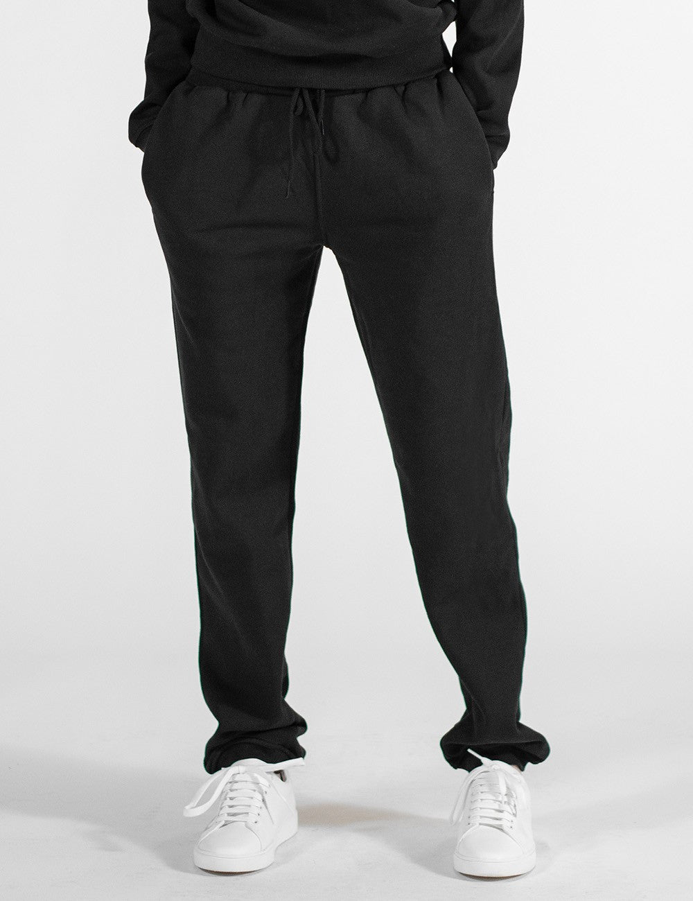 The image shows a front pose of a pair of black sweatpants with an elastic waistband, side pockets.