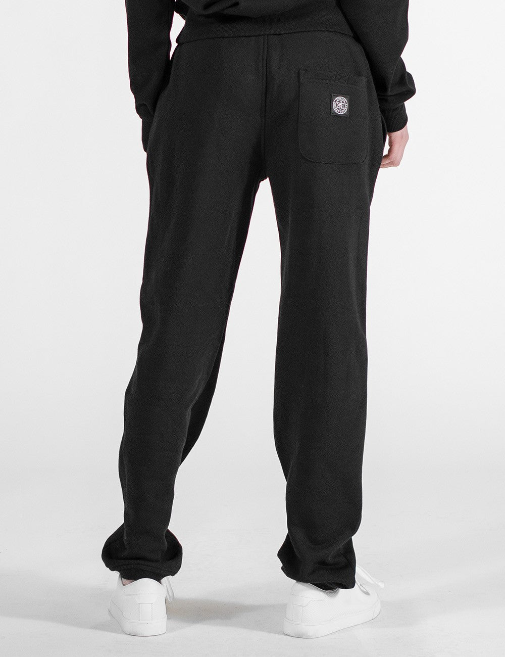The image shows a pair of black sweatpants with an elastic waistband, side pockets, and a back pocket featuring a round Rocket Science label patch.