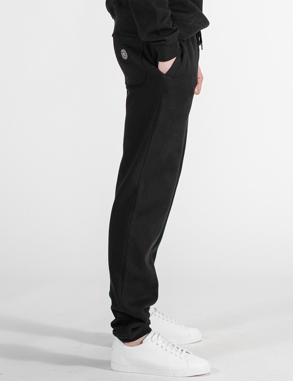 This image shows a side pose of a person wearing a casual black crew-neck sweatshirt and matching black sweatpants, paired with white sneakers.