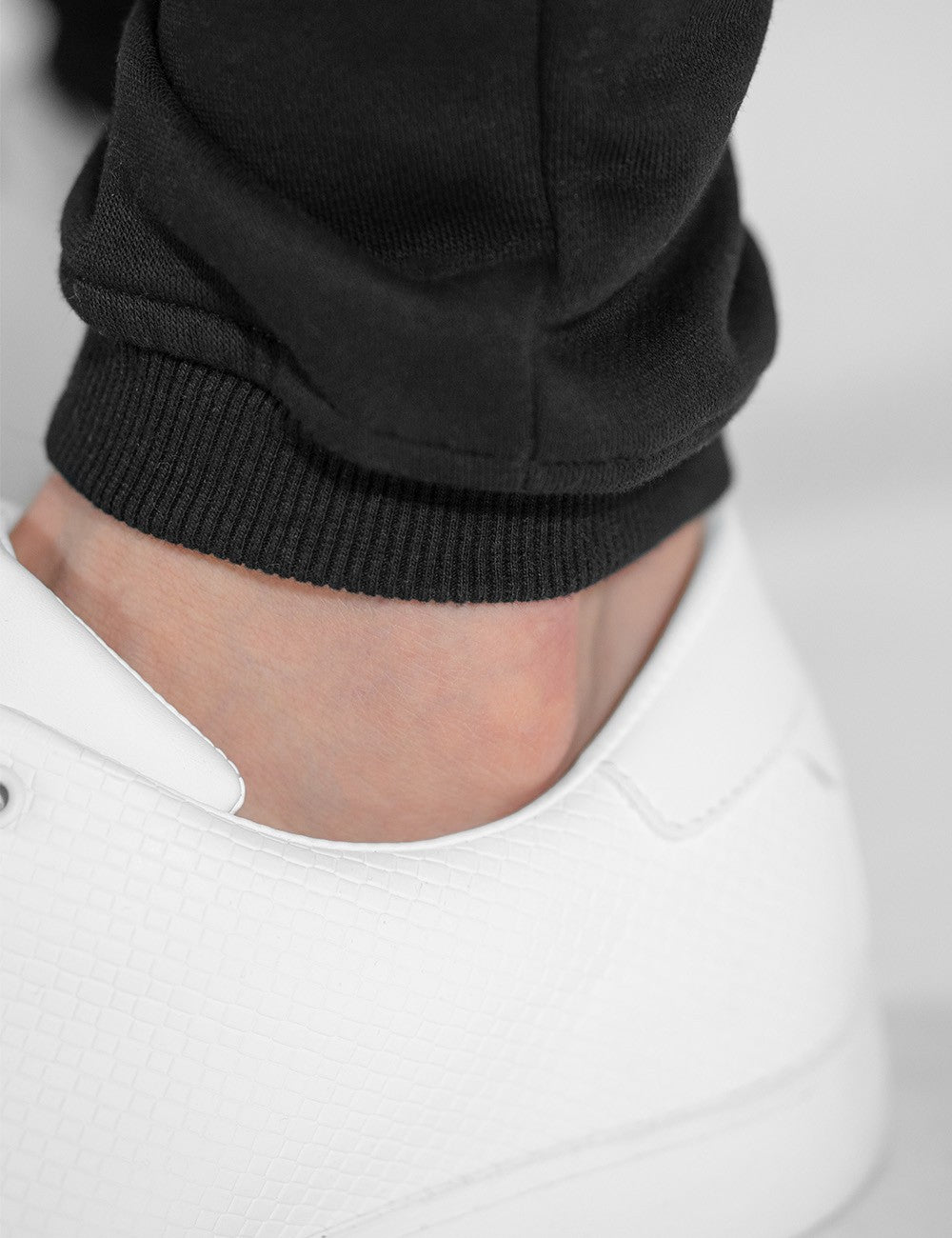 This image shows a pair of black sweatpants with ribbed cuffs worn with white sneakers.