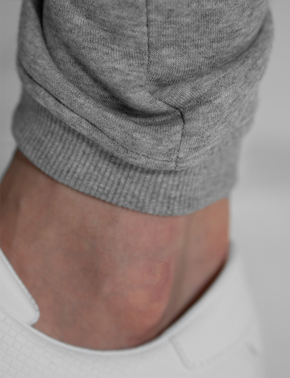 A close-up shot of a person's lower leg and ankle, showcasing the ribbed cuff of Rocket Science light grey heather jogger pants paired with clean white sneakers.