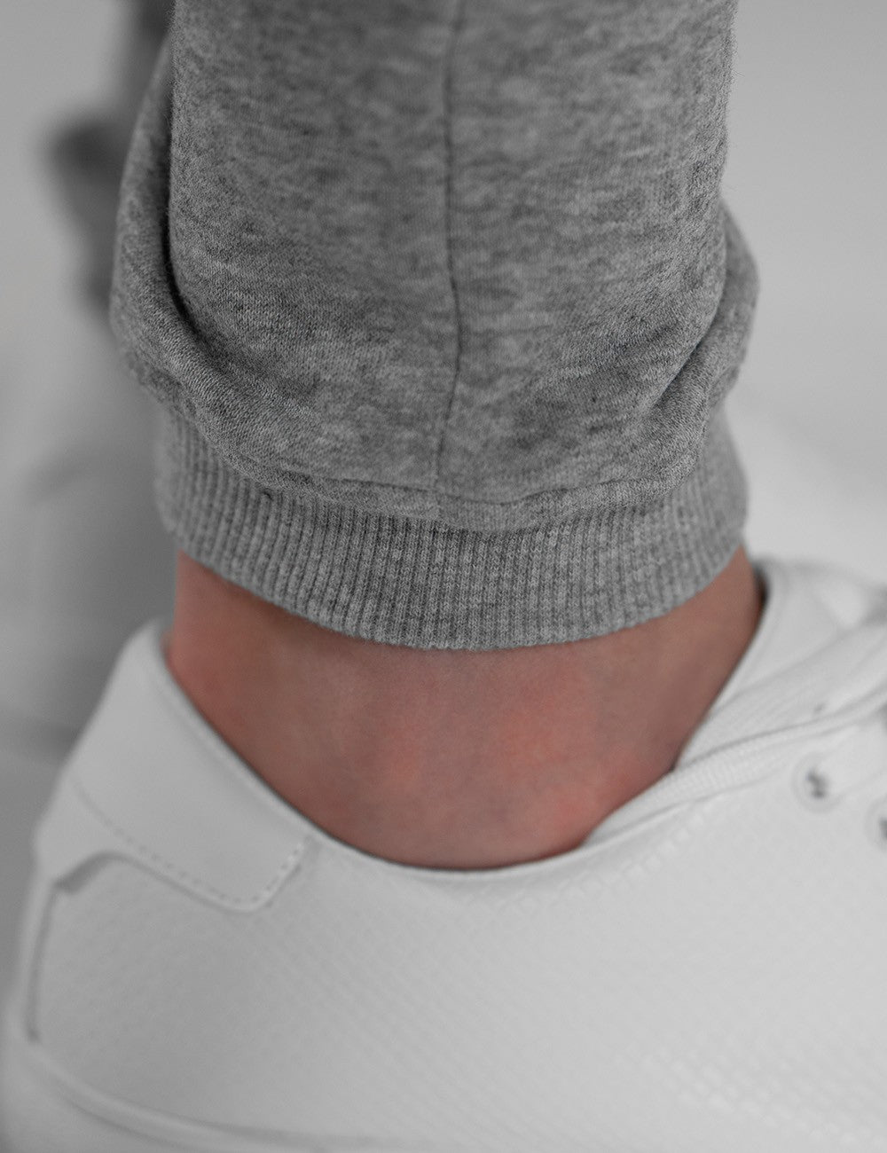 The image shows grey sweatpants with ribbed elastic cuffs paired with white sneakers.