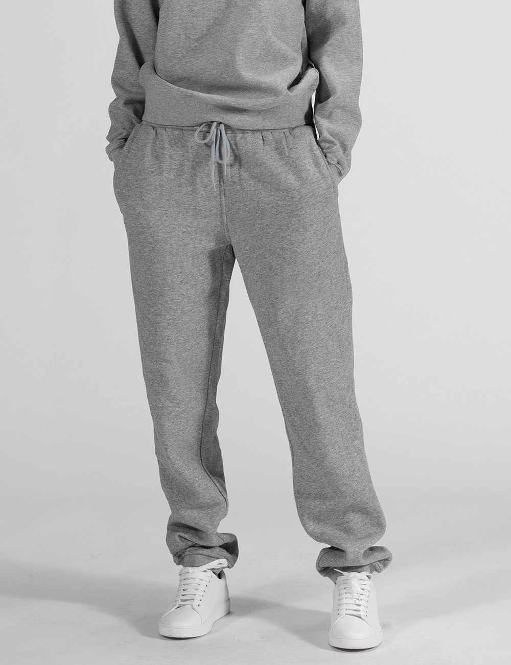 A model wearing Rocket Science Sweatpants in a heather grey colorway, featuring a relaxed, classic fit. The sweatpants have a flexible elastic waistband adjusted by a matching grey drawcord, side pockets, and cinched elastic cuffs at the ankles.