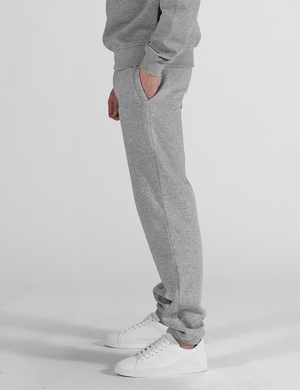 A pair of heather grey sweatpants with a relaxed, straight-leg fit and classic elasticated ankle cuffs. They are styled as part of a matching loungewear set and paired with clean white leather sneakers.