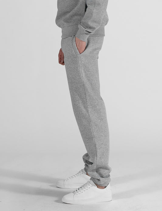 A pair of heather grey sweatpants with a relaxed, straight-leg fit and classic elasticated ankle cuffs. They are styled as part of a matching loungewear set and paired with clean white leather sneakers.