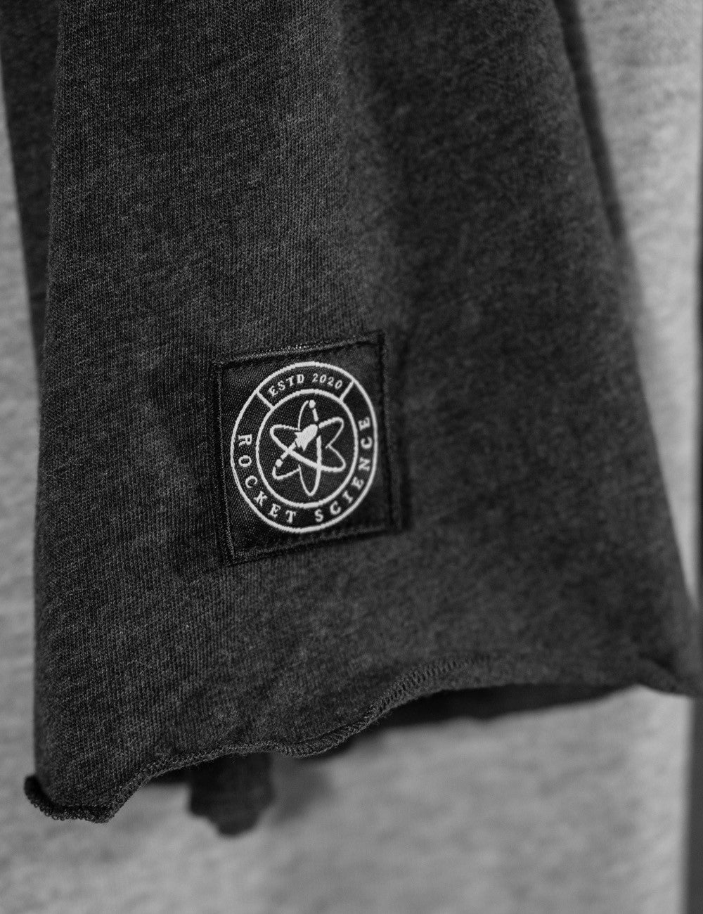 Close-up of a dark charcoal gray heathered fabric sleeve with a square black patch featuring a white atom symbol and the text 'ROCKET SCIENCE ESTD 2020'.