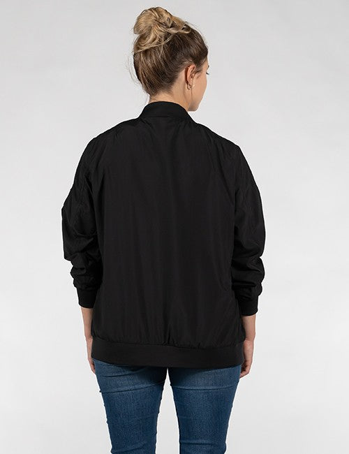 A woman viewed from the back wearing a black bomber jacket and blue jeans against a light gray studio background.