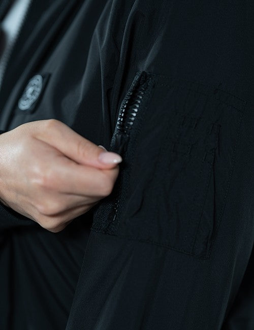 Close-up of a person's hand opening a black zippered pocket on a black jacket.