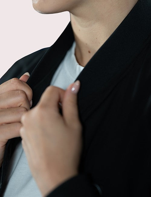 Close-up of a person wearing a black jacket over a white crewneck shirt, adjusting the collar with both hands.