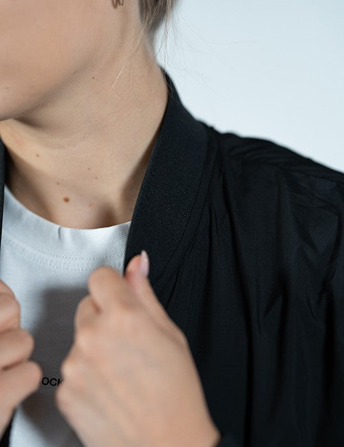 Close-up of a person wearing a black lightweight jacket or overshirt over a white crew-neck t-shirt, with hands adjusting the collar of the outer layer.