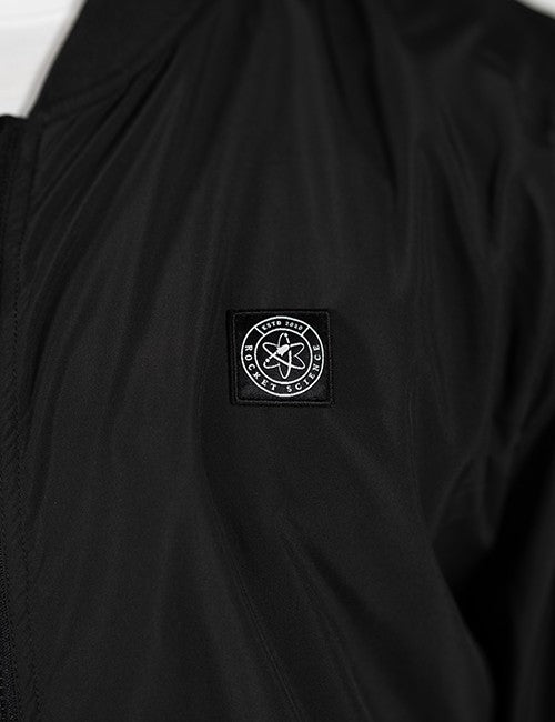 Close-up of a black jacket or overshirt with a circular black-and-white Rocket Science logo patch on the chest. 