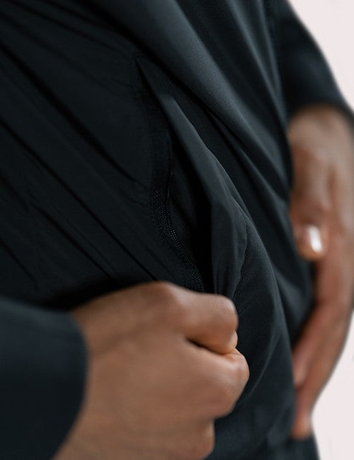 Close-up of a person wearing a black long-sleeve top or dress, pulling the fabric slightly to show the texture and drape of the material.