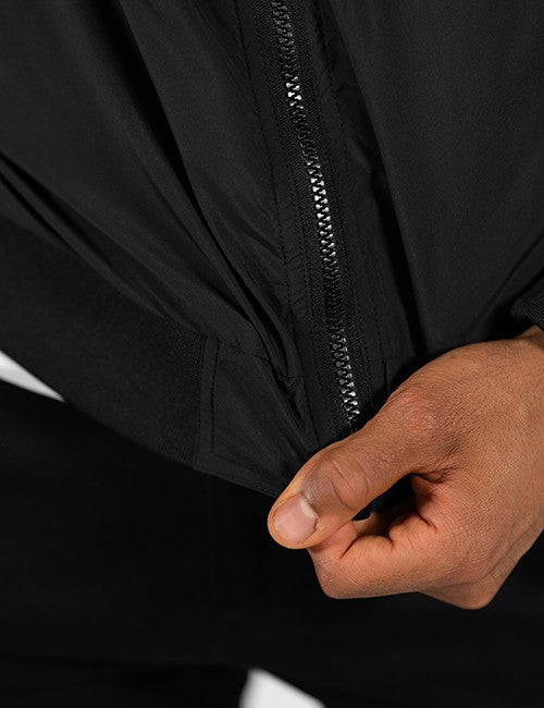 Close-up of a person's hand pulling a black zipper on a black jacket, showing the texture of the fabric and the metallic zipper teeth.