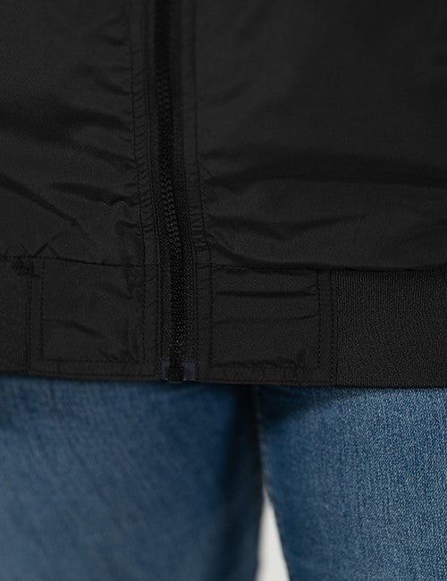 Close-up of a black puffer jacket with a front zipper and ribbed hem, worn over blue jeans.