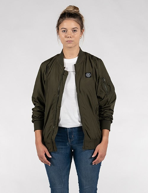 A woman modeling an olive green bomber jacket over a white t-shirt and blue jeans, standing against a light gray studio background.