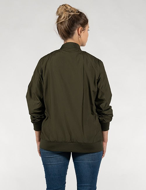 A woman viewed from the back wearing an olive green bomber jacket and blue jeans against a light gray studio background.