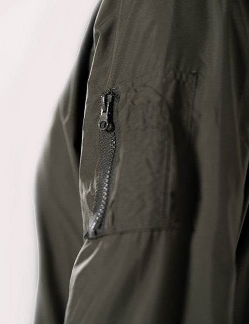 An olive green bomber jacket sleeve featuring a zippered utility pocket with a dark metallic zipper pulls.
