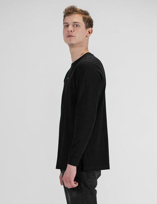 This image shows a side pose of a young man wearing a plain black long-sleeve crewneck shirt with a small logo Rocket Scientist print on the chest 