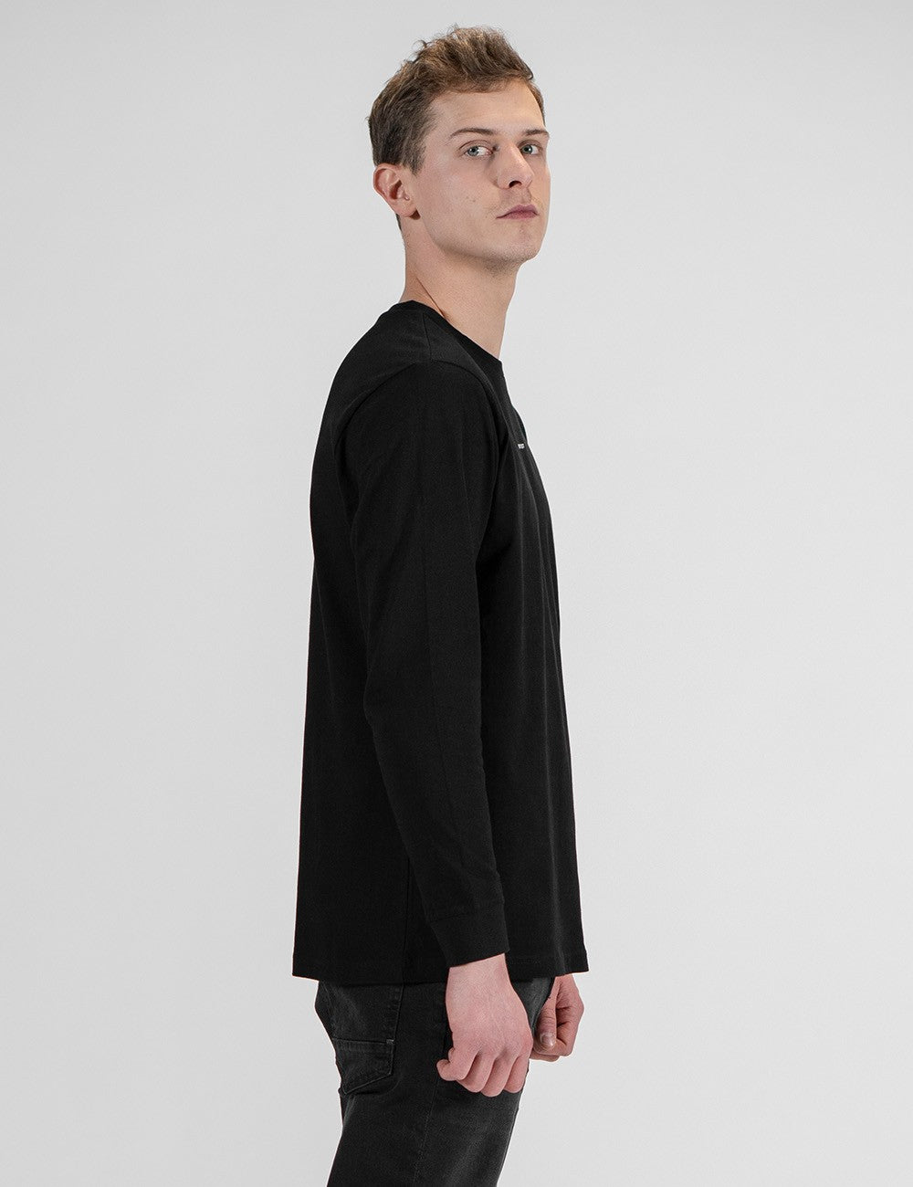 This image shows a side pose of a young man wearing a plain black long-sleeve crewneck shirt with a small logo Rocket Scientist print on the chest 