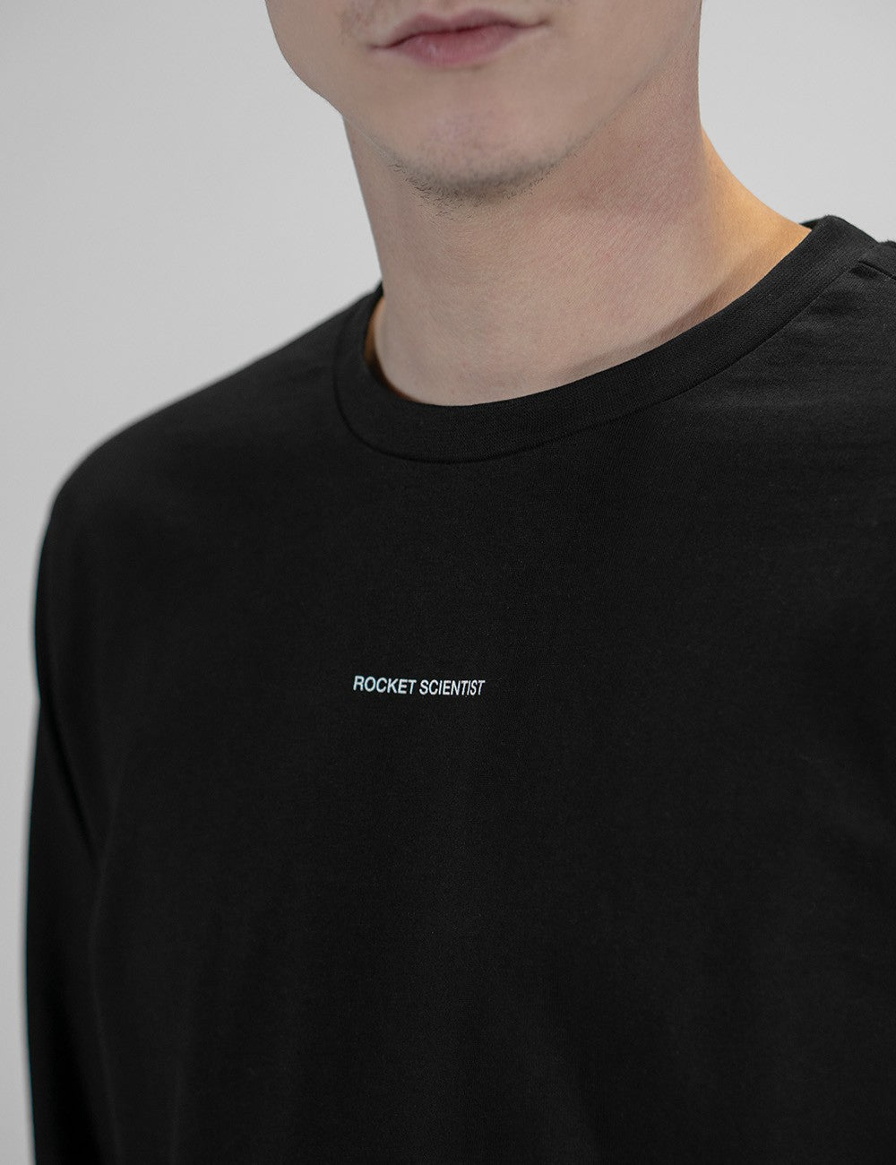 This image shows close view of  a plain black long-sleeve crewneck shirt with a small logo Rocket Scientist print on the chest 