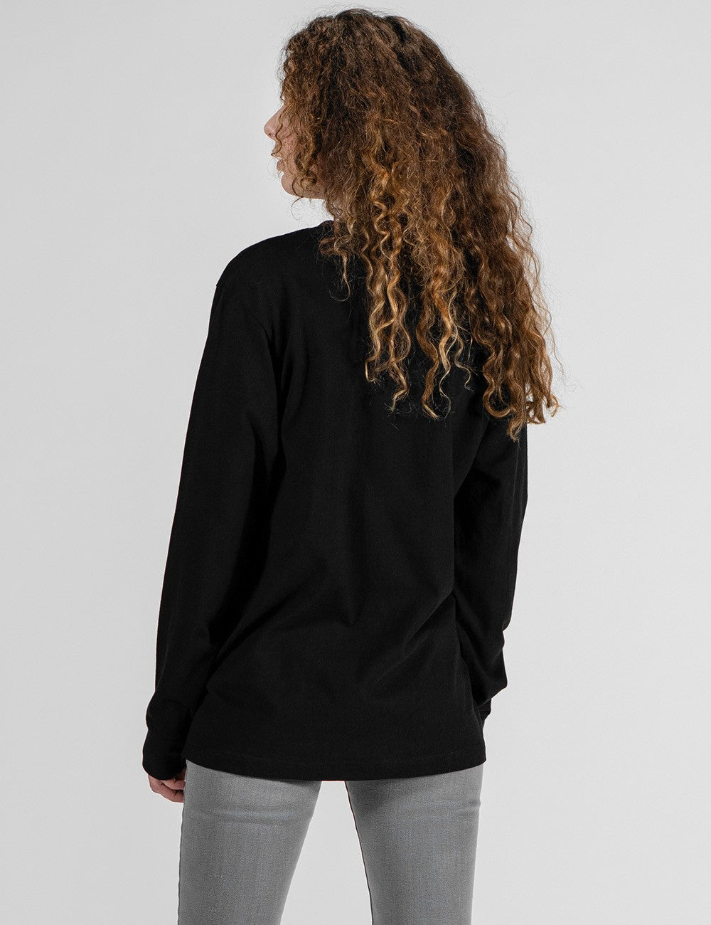 This image shows a rear pose of a young man wearing a plain black long-sleeve crewneck shirt .