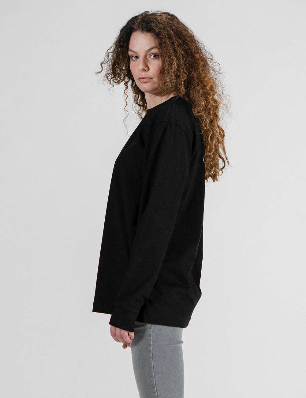 This image shows a side pose of a young man wearing a plain black long-sleeve crewneck shirt with a small logo Rocket Scientist print on the chest 