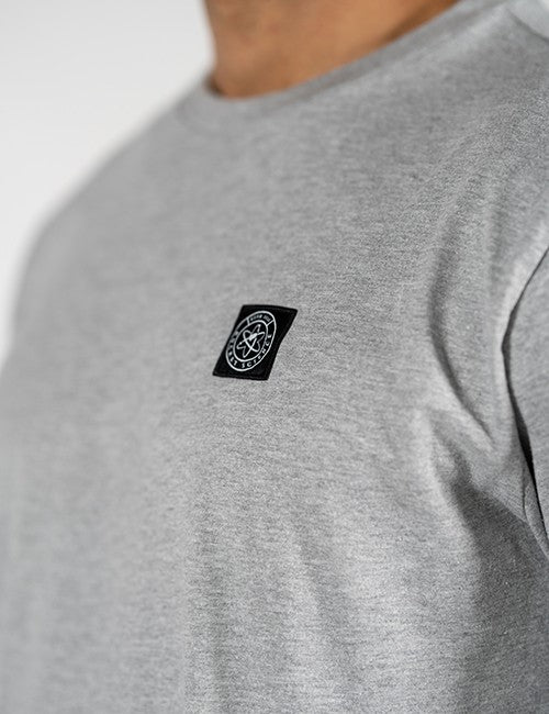 Close-up of a person wearing a heather gray crewneck t-shirt with a small black rectangular chest patch featuring a white Rocket Science circular logo.