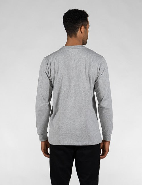 A man viewed from the back wearing a light gray long-sleeve t-shirt and black pants, standing against a light gray studio background.
