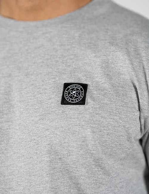 Close-up of a person wearing a heather gray crewneck t-shirt with a black square chest patch featuring a white Rocket Science logo.