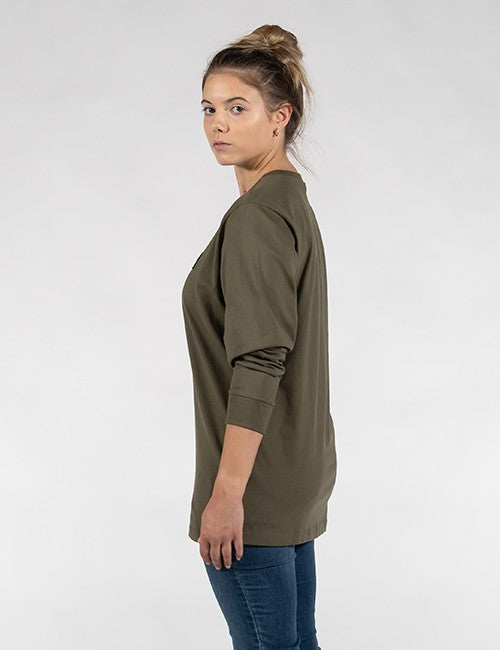 A woman with dark hair tied in a high bun stands in a side-profile view against a plain, light grey background. She wears a loose-fitting, long-sleeved olive green crewneck shirt with ribbed cuffs and blue jeans.